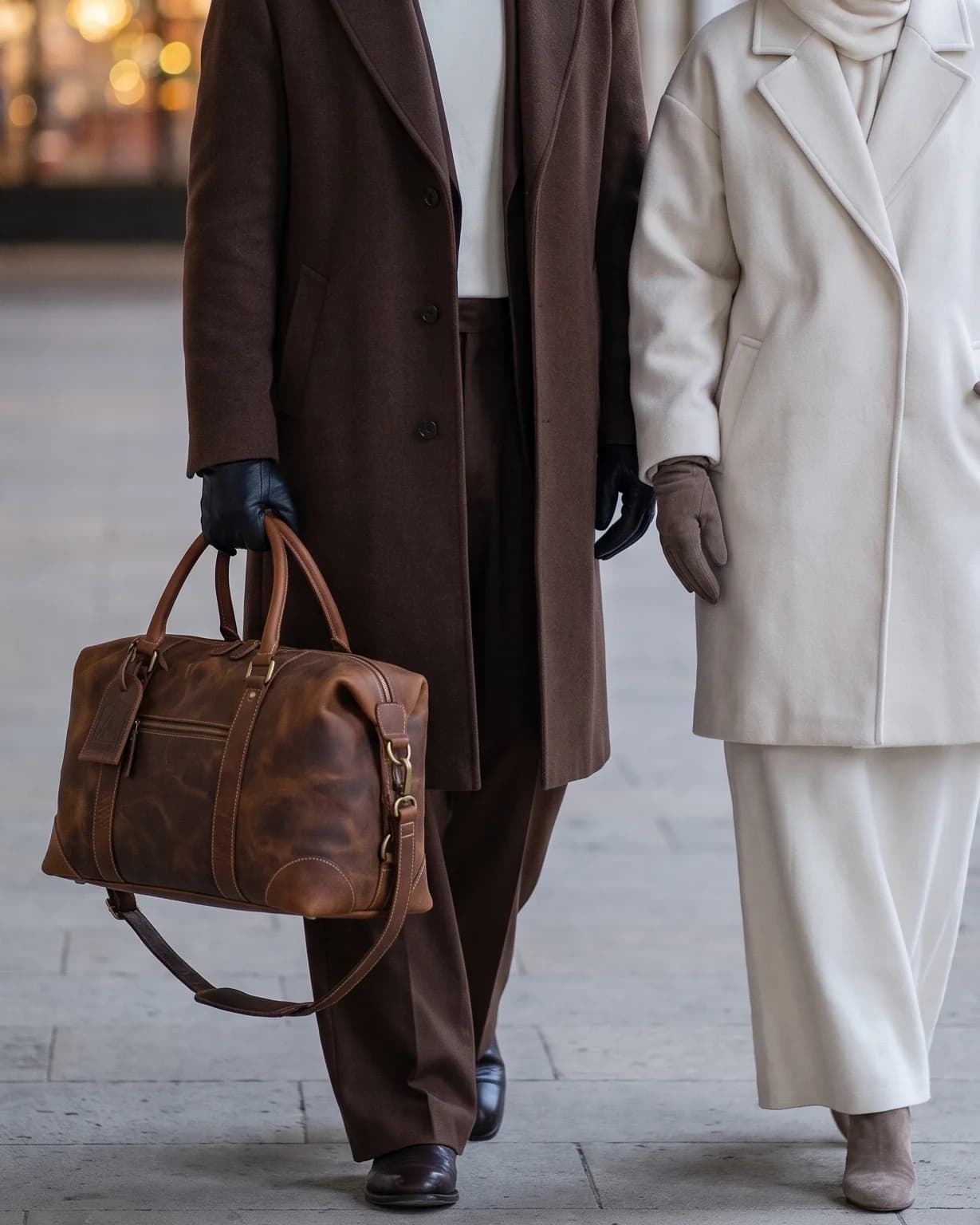 Gloved hand carrying the tan Art 201 full-grain leather duffle by its rolled handles